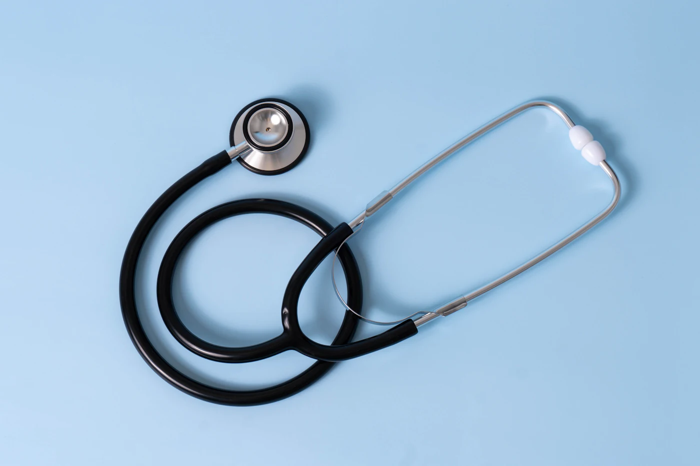 A black medical stethoscope on a light blue background — photo by Etactics Inc on Unsplash